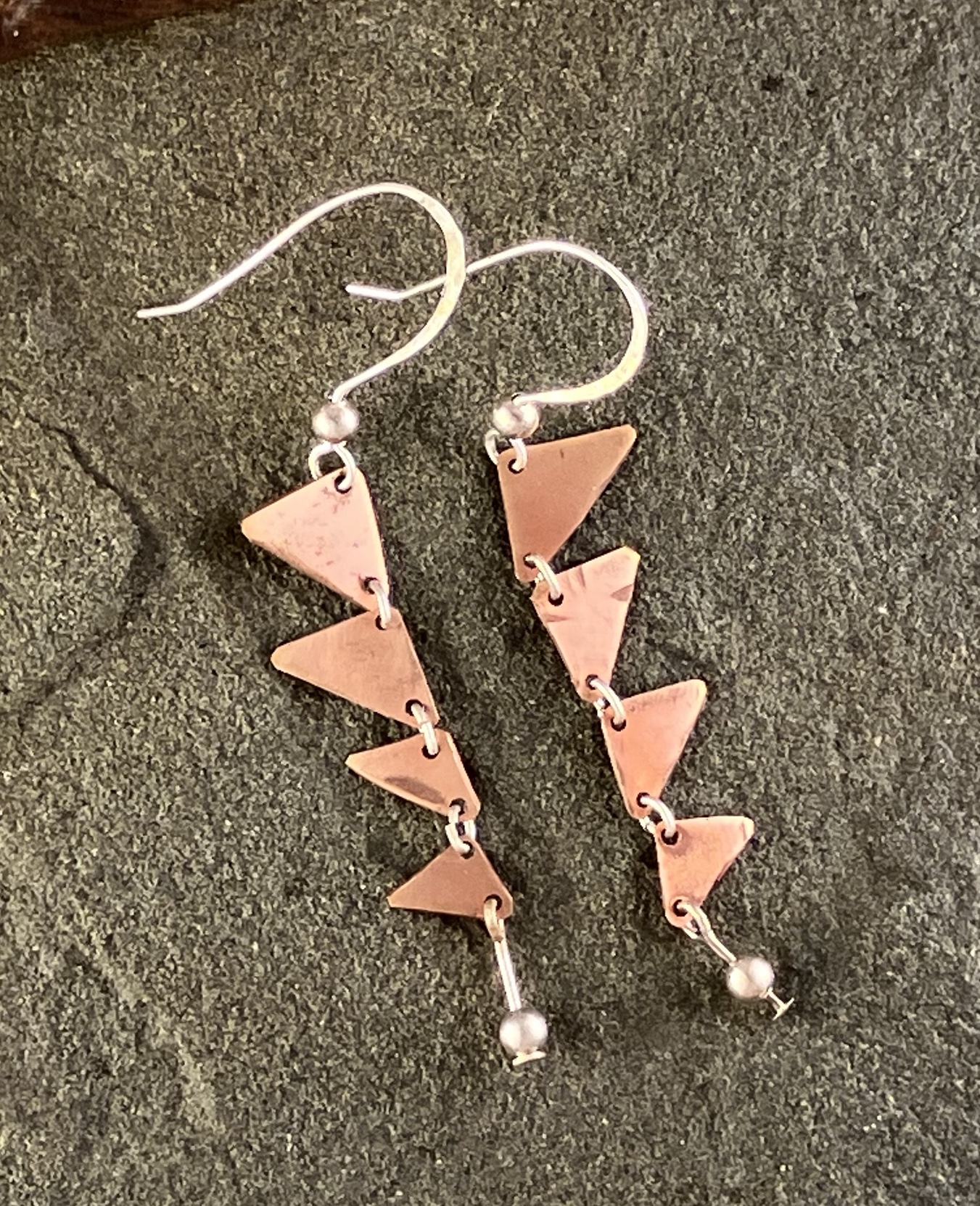 Earrings of linked small copper triangles hanging with silver bead